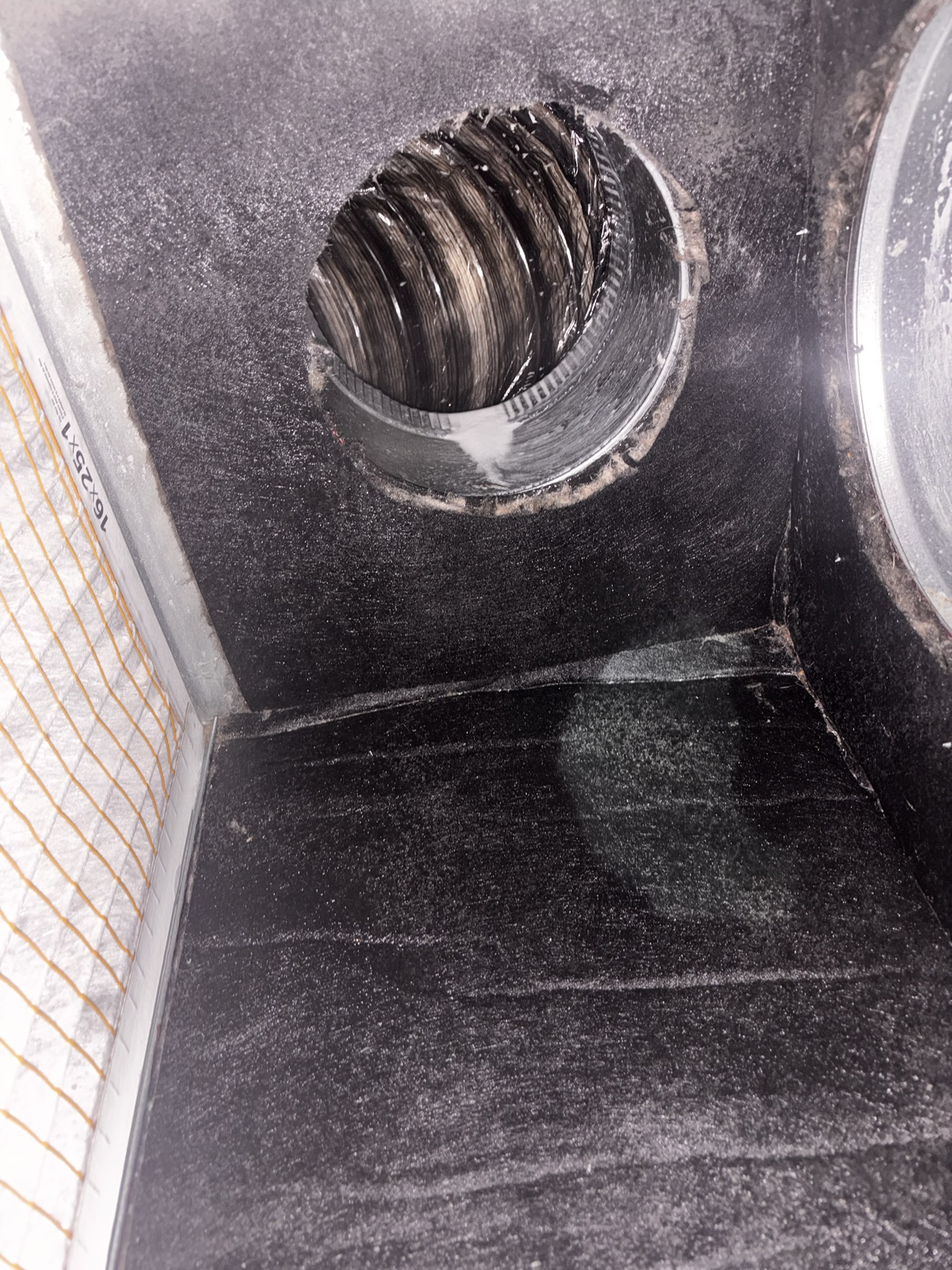 A close-up view of the inside of an HVAC duct showing a round metallic vent, ductwork, and an air filter on the left side—demonstrating the thorough results of a professional air duct cleaning service.