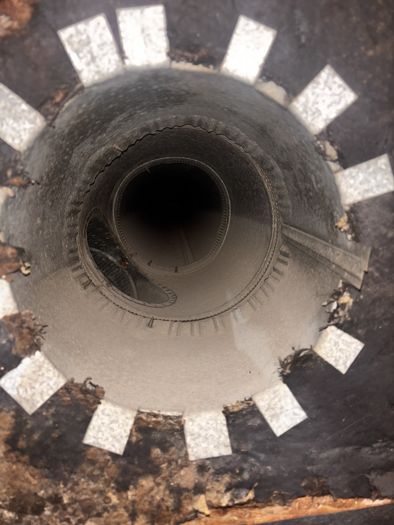 Close-up view looking down into a cylindrical metal pipe with white rectangular markings around the rim and visible dust and debris inside.