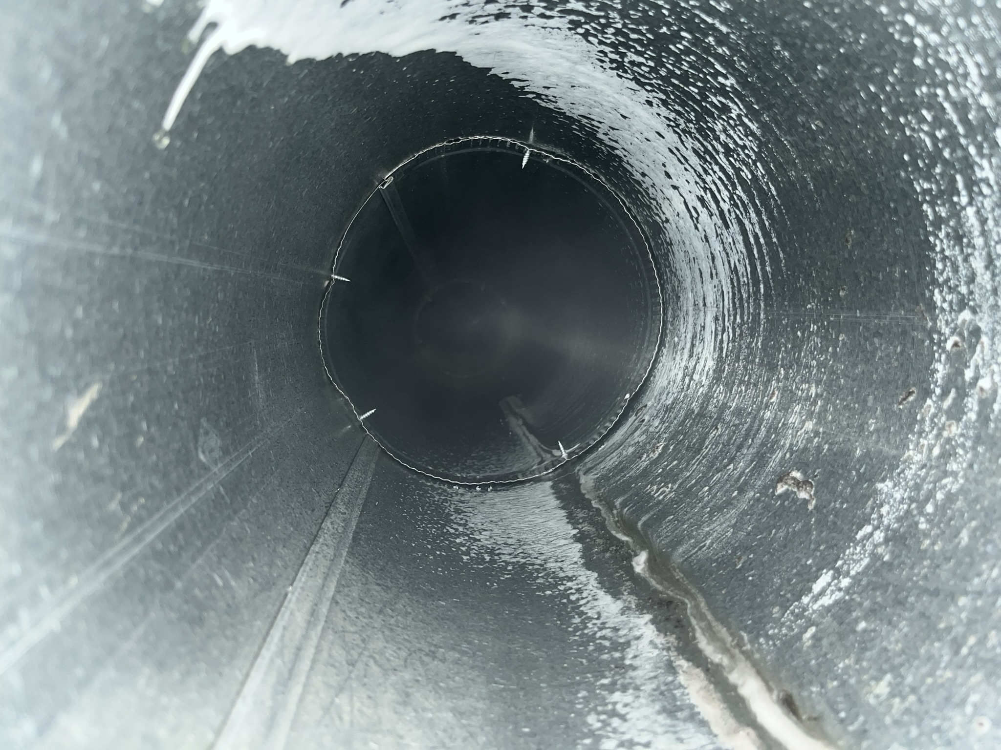 Interior view of a cylindrical metal duct or pipe with visible dust and grime buildup along the inner surface.
