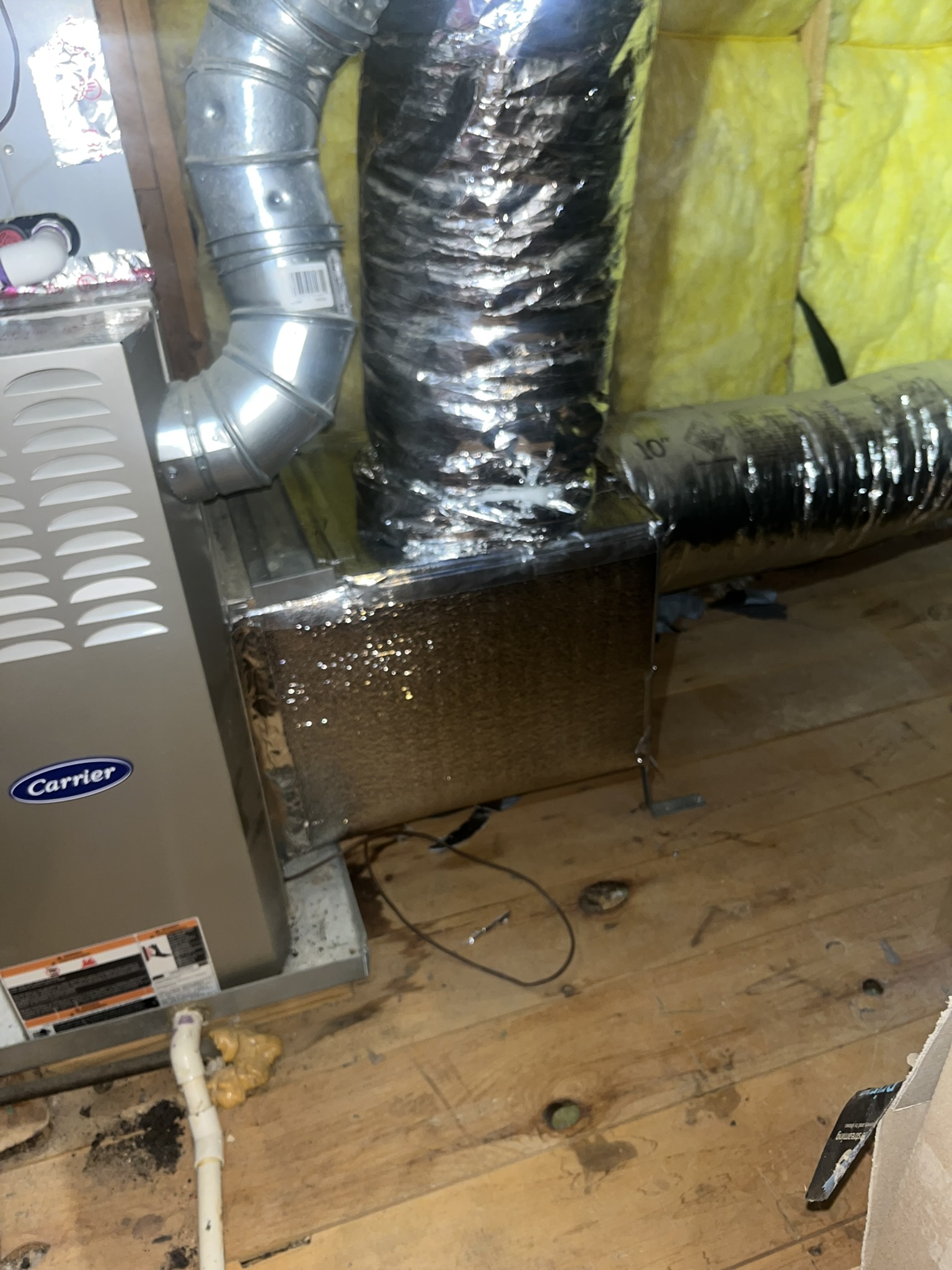 Furnace system with attached ductwork in an unfinished room with exposed insulation and wooden floor.