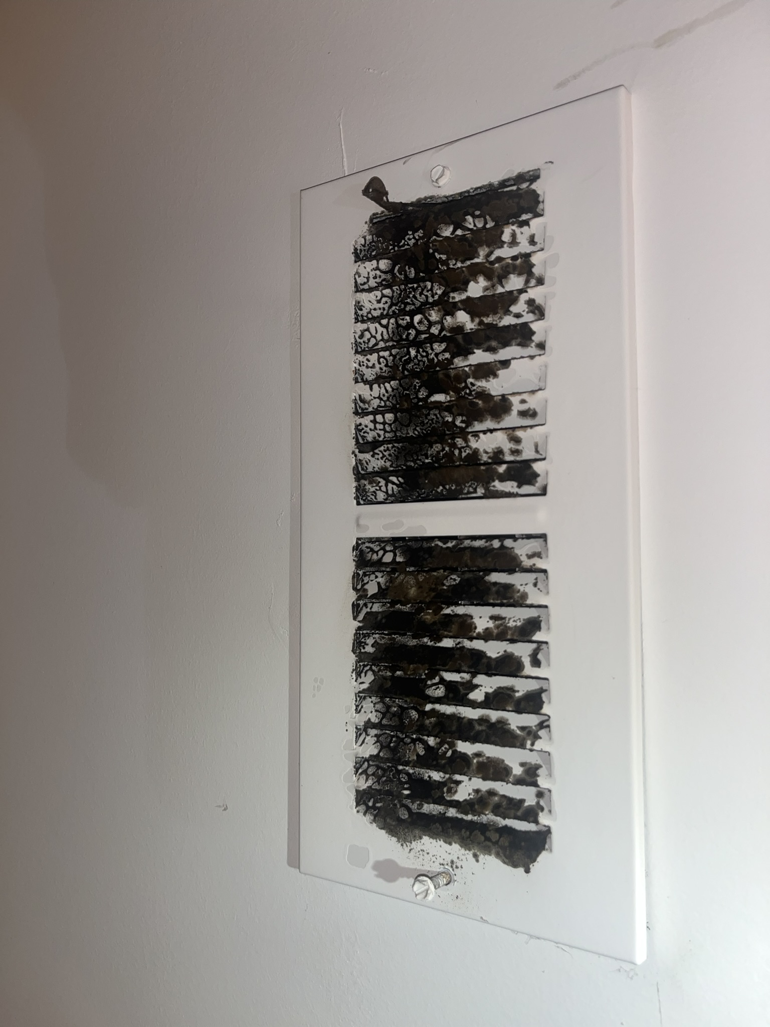 A white wall vent cover with two grilles, both covered in a thick layer of black soot or dirt—an obvious sign that an air duct cleaning service is needed.